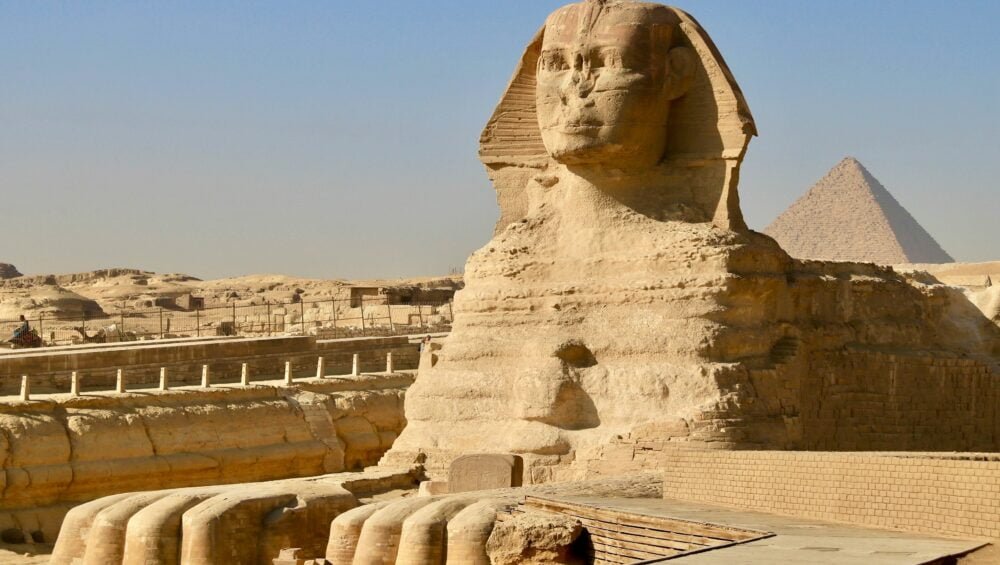 A photo of the Great Sphinx of Giza and the Great Pyramid of Giza, showcasing the massive limestone statue and the pyramid in the background.