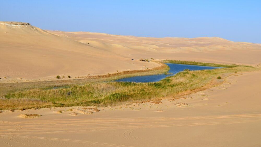 A panoramic view of the Siwa Oasis in Egypt, showcasing salt pans, mining operations, and a small pool of turquoise water.