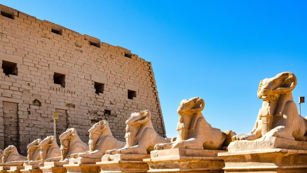 A photo of the Avenue of Sphinxes at Karnak Temple, showcasing rows of ram-headed sphinxes leading towards the temple entrance.