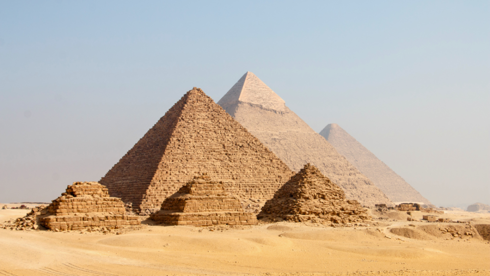 A photo of the Great Pyramid of Giza and the surrounding pyramids in the Giza Necropolis, showcasing the massive size and the surrounding desert landscape.