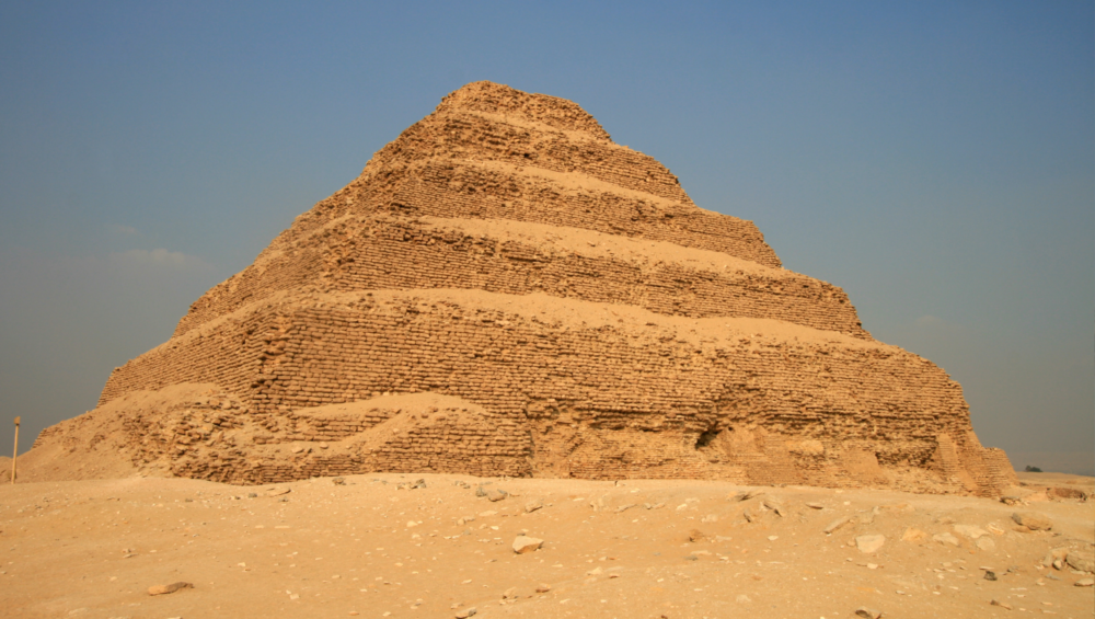 A photo of the Step Pyramid of Djoser in the Saqqara Necropolis, showcasing its unique stepped design and the surrounding desert landscape.