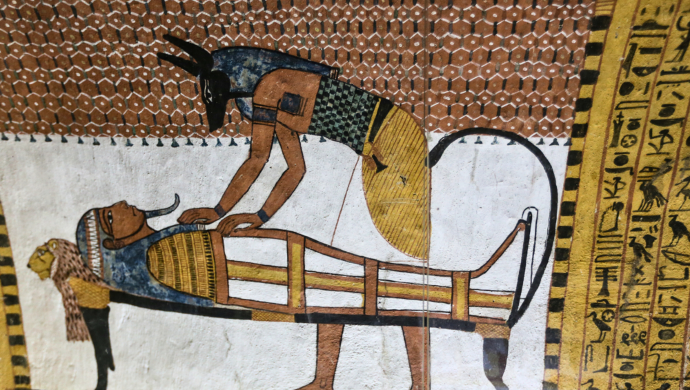 A wall painting from the Tomb of Sennedjem in Deir el-Medina, Luxor, Egypt, showing Anubis performing the mummification ritual on a deceased person.