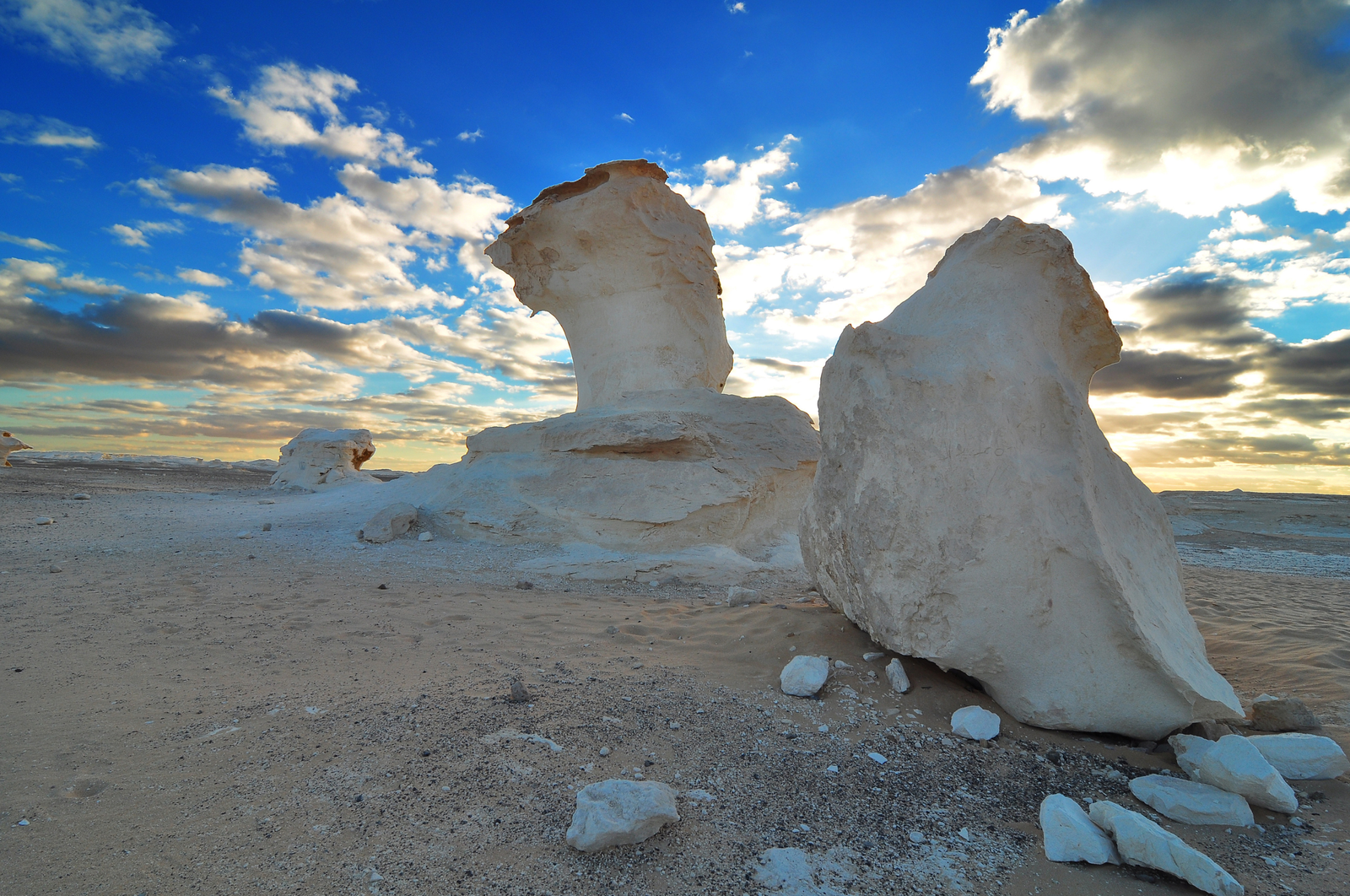  A photo of the White Desert National Park in Egypt, showcasing two large white rock formations standing tall against a blue sky with fluffy clouds.