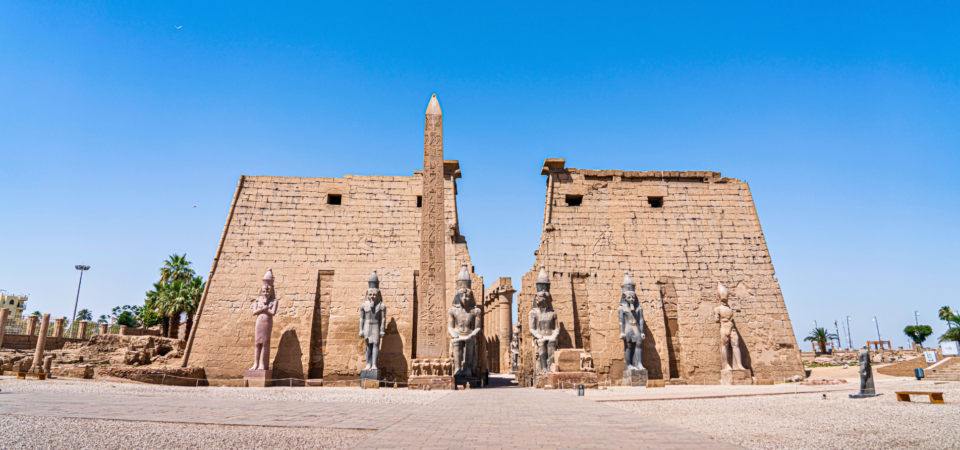 A panoramic view of Luxor Temple, showcasing the massive pylons, the statues of pharaohs, and the obelisk standing in front of the temple.