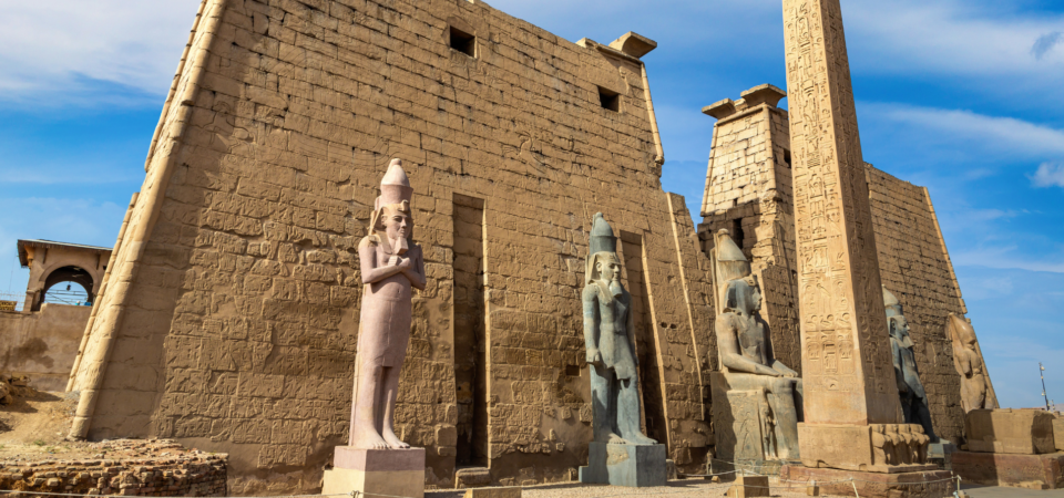 A photo of Luxor Temple in Luxor, Egypt, showcasing the colossal statues of pharaohs, the temple's sandstone facade, and a towering obelisk.