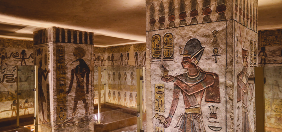 A photo of the interior of the Tomb of Ramses III in the Valley of the Kings, showcasing the colorful wall paintings, the sarcophagus, and the pillars adorned with hieroglyphs.