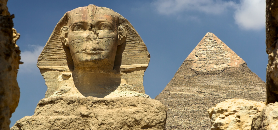 Close-up view of the face of the Great Sphinx with a pyramid in the background.