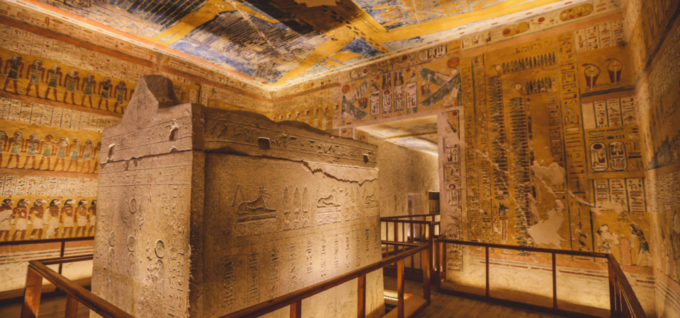 The interior of the Tomb of Ramses IV in the Valley of the Kings, featuring a large sarcophagus and colorful wall paintings depicting religious scenes.