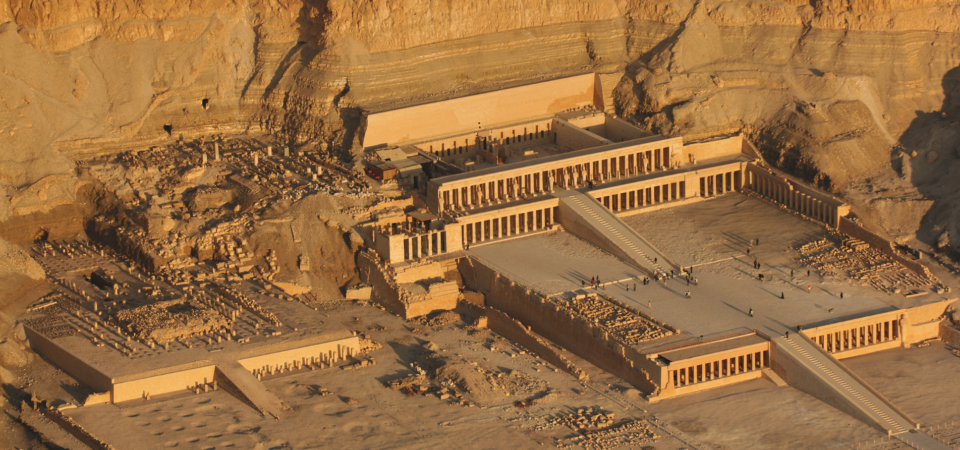 An aerial view of the Mortuary Temple of Hatshepsut in Deir el-Bahari, showcasing its terraced design and its integration into the surrounding cliffs.