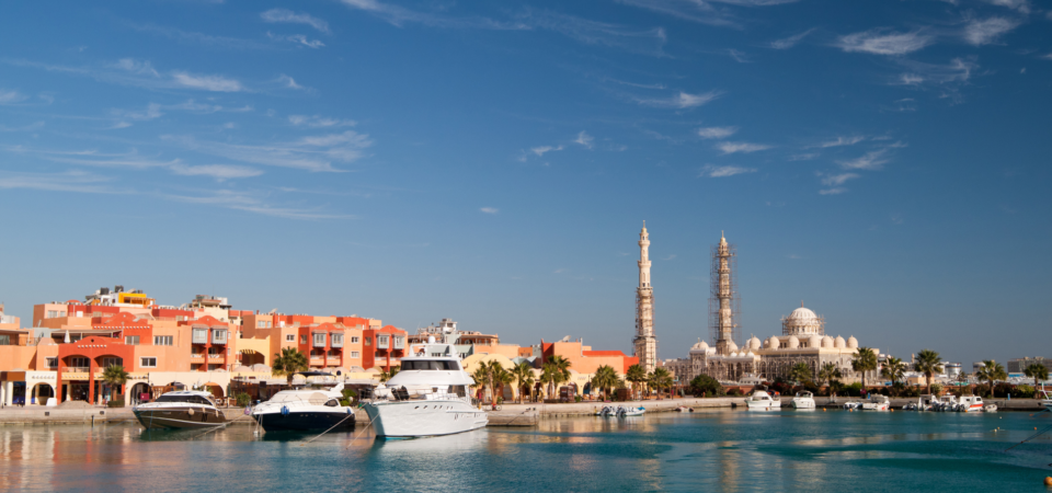 A view of Al Mina Mosque in Hurghada, Egypt, from the sea. The mosque is a large, white structure with a prominent dome and minarets.