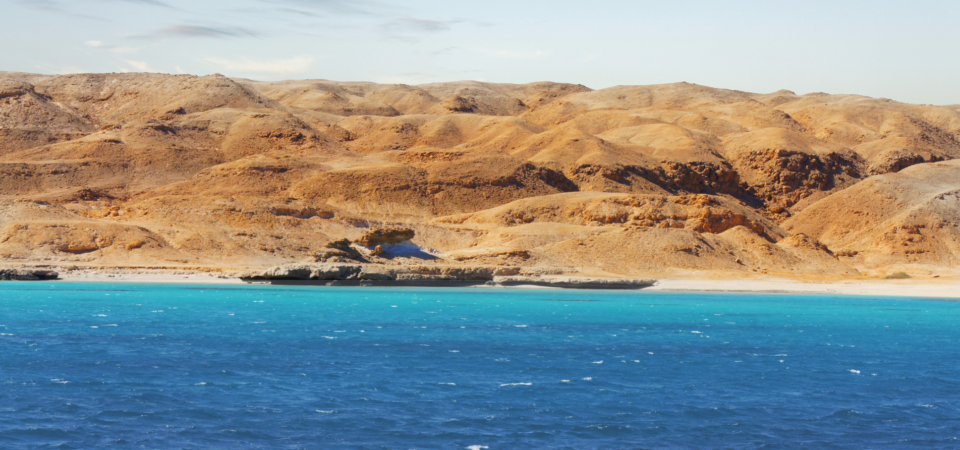 A panoramic view of the Red Sea coastline in Egypt, featuring arid desert mountains, rocky cliffs, and turquoise water.