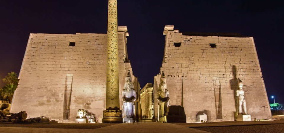 Luxor Temple front gate illuminated at night, with towering pylons and statues.