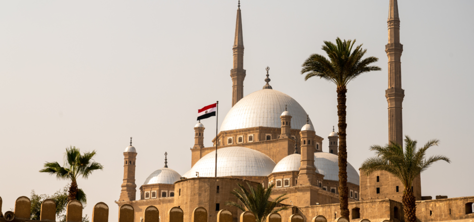 A photo of the Citadel of Saladin in Cairo, Egypt, featuring a large, white dome mosque with minarets and palm trees.