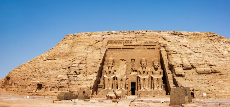 A photo of the Great Temple of Abu Simbel, showcasing the four colossal statues of Ramses II guarding the entrance and the temple's impressive facade carved into the mountainside.