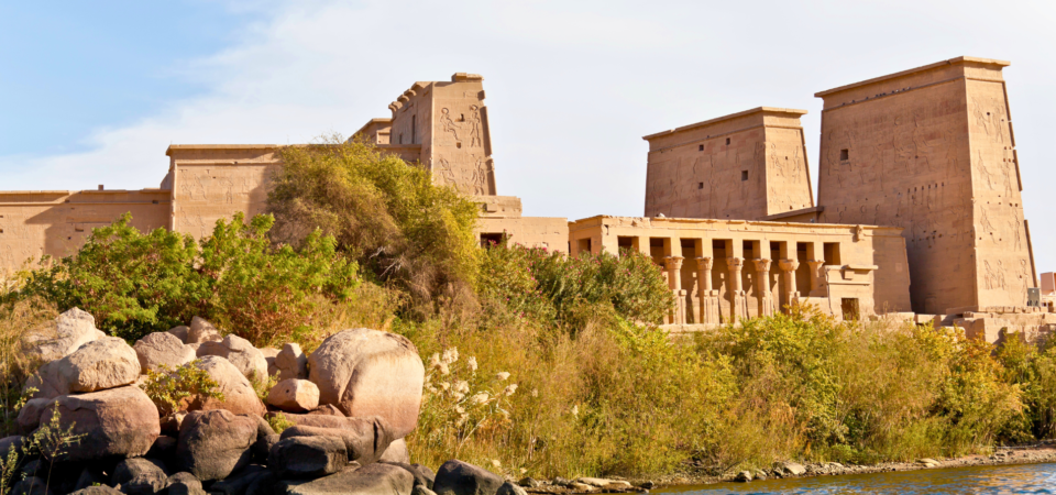 Philae Temple viewed from the Nile, surrounded by water and lush greenery.