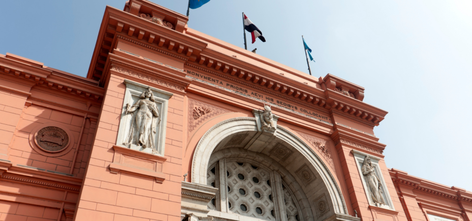 A close-up of the Egyptian Museum in Cairo, showcasing its ornate facade, statues, and the Egyptian flag flying above.
