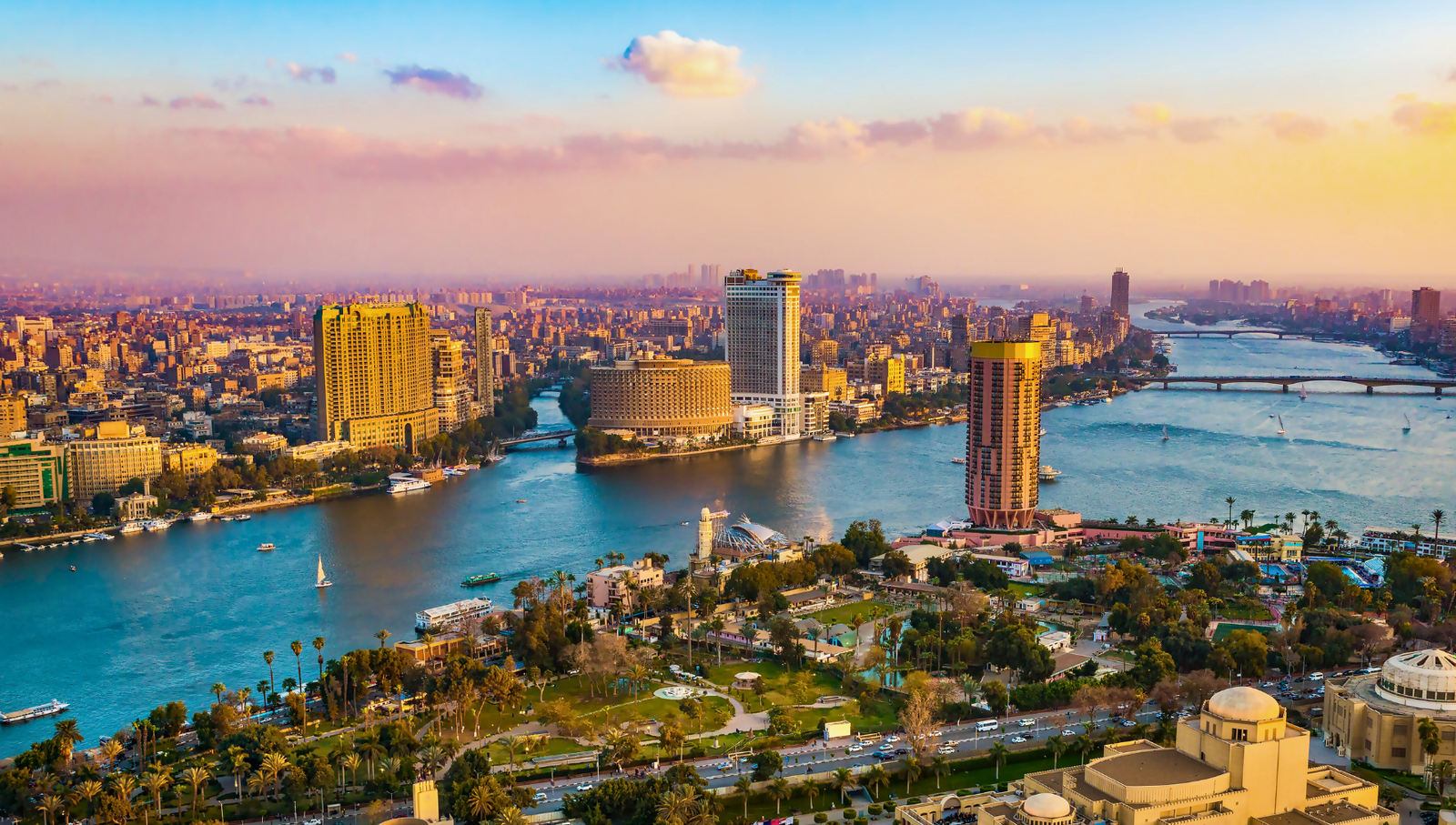 A panoramic view of Cairo, Egypt, at sunset, showcasing the city's skyline, the Nile River, and the surrounding urban landscape.