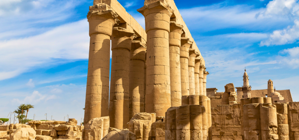 A photo of the Hypostyle Hall at Luxor Temple, showcasing the towering columns, the hieroglyphics on the walls, and the minaret of Abu Haggag Mosque in the background.
