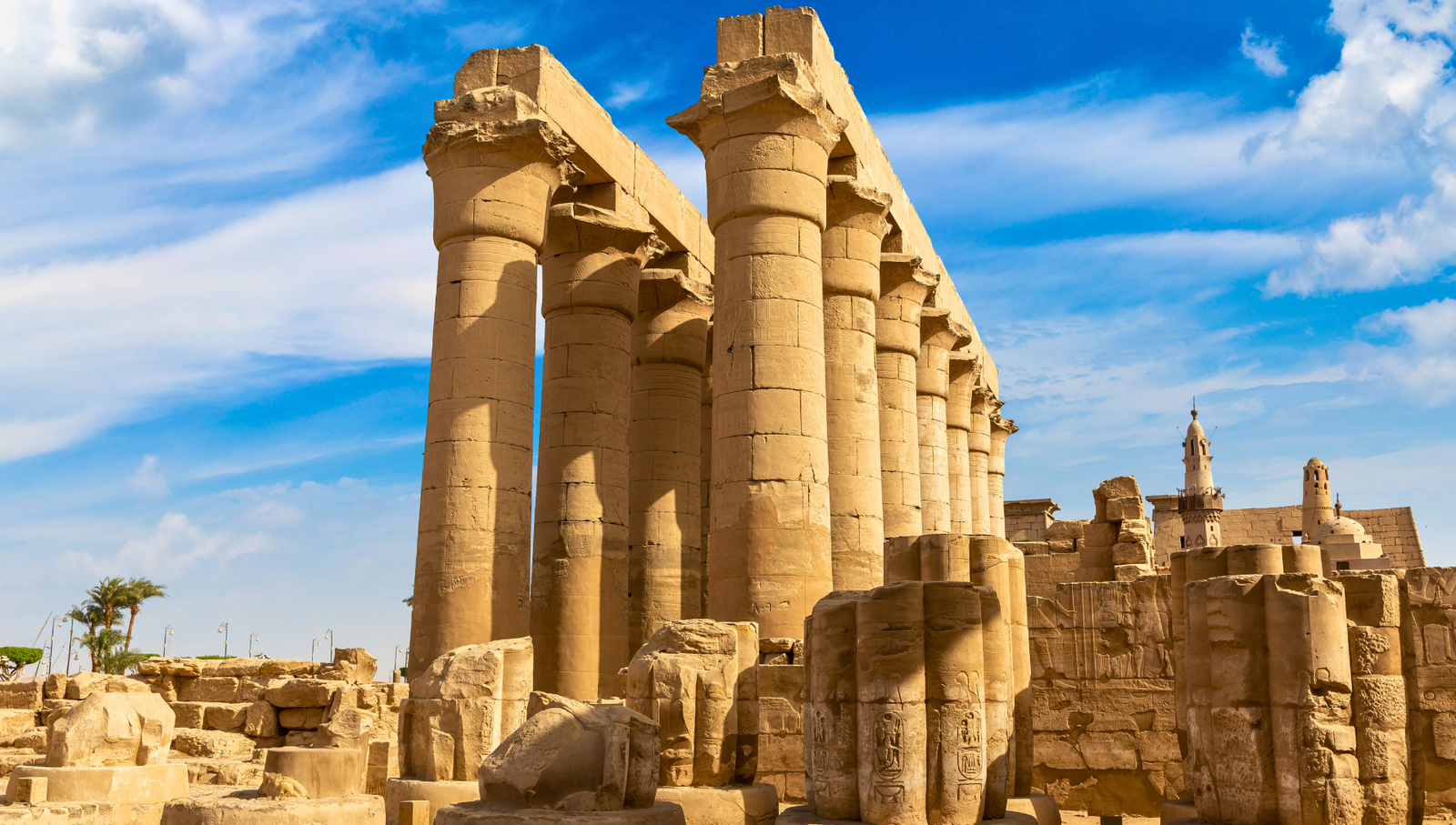 A photo of the Hypostyle Hall at Luxor Temple, showcasing the towering columns, the hieroglyphics on the walls, and the minaret of Abu Haggag Mosque in the background.