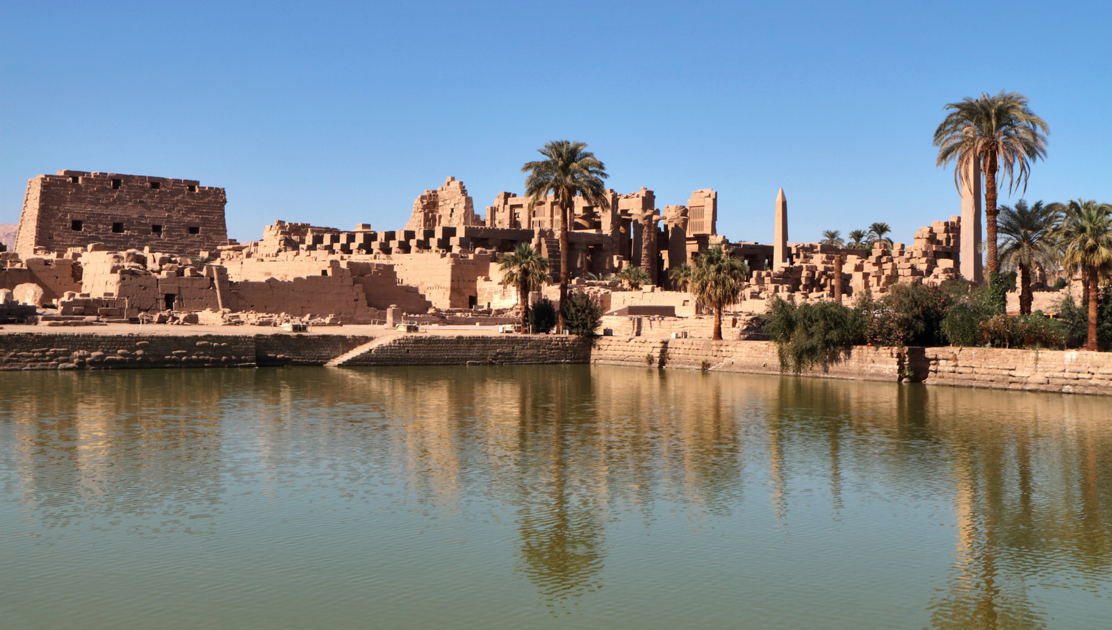 A photo of Karnak Temple in Luxor, Egypt, showcasing the massive temple complex with its towering columns and pylons, reflected in a calm pool of water.