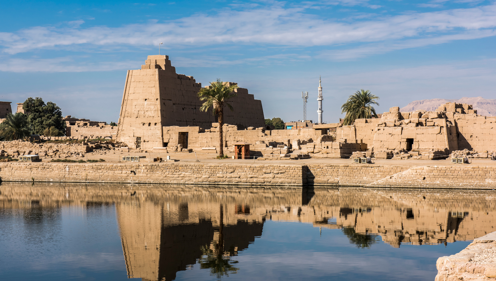 A photo of the Karnak Temple complex in Luxor, Egypt, with a calm pool of water reflecting the ancient ruins.