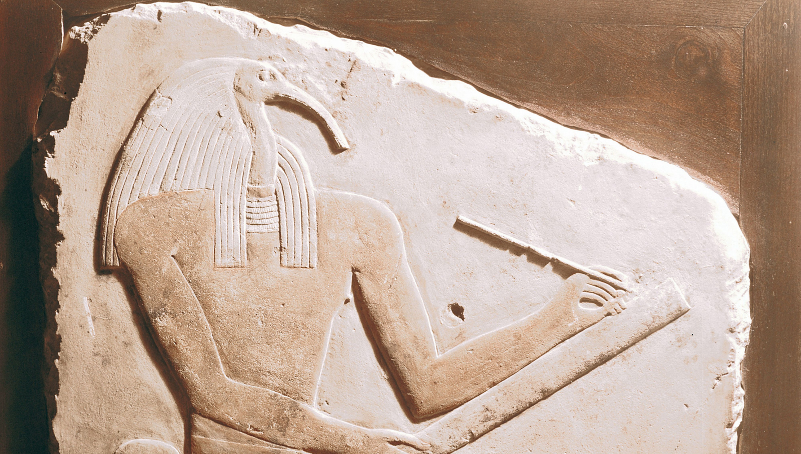 A stone relief depicting Thoth, the ibis-headed god of wisdom and magic, holding a scribe's palette and stylus.