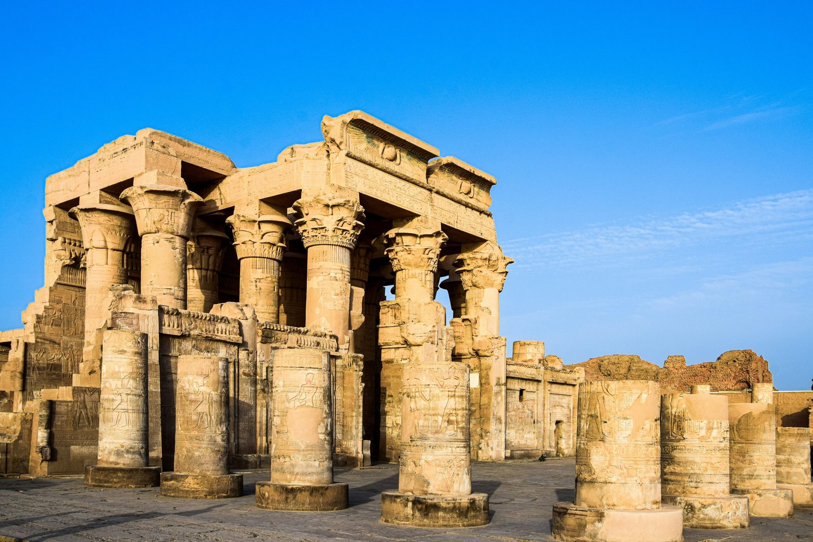 A panoramic view of the Temple of Kom Ombo in Aswan, Egypt, showcasing its double pylons, towering columns, and the Nile River in the background.