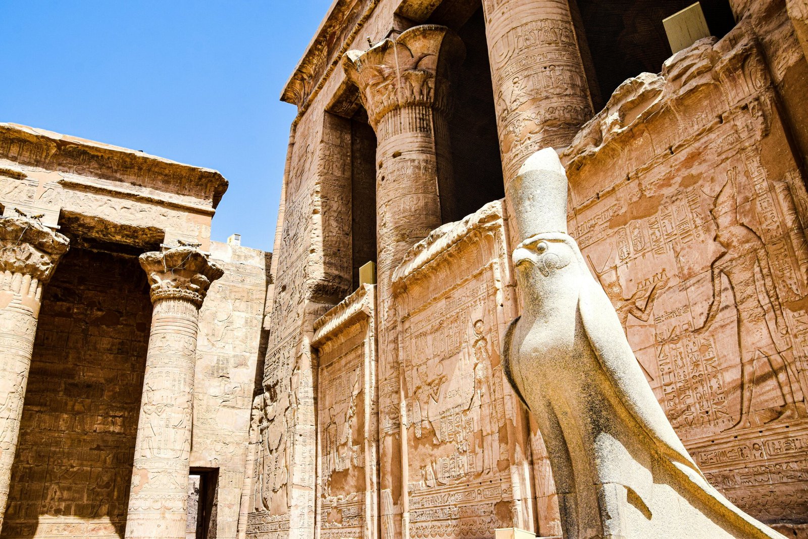 A photo of the Temple of Edfu, showcasing the massive pylons, decorated with hieroglyphs, and a statue of Horus.