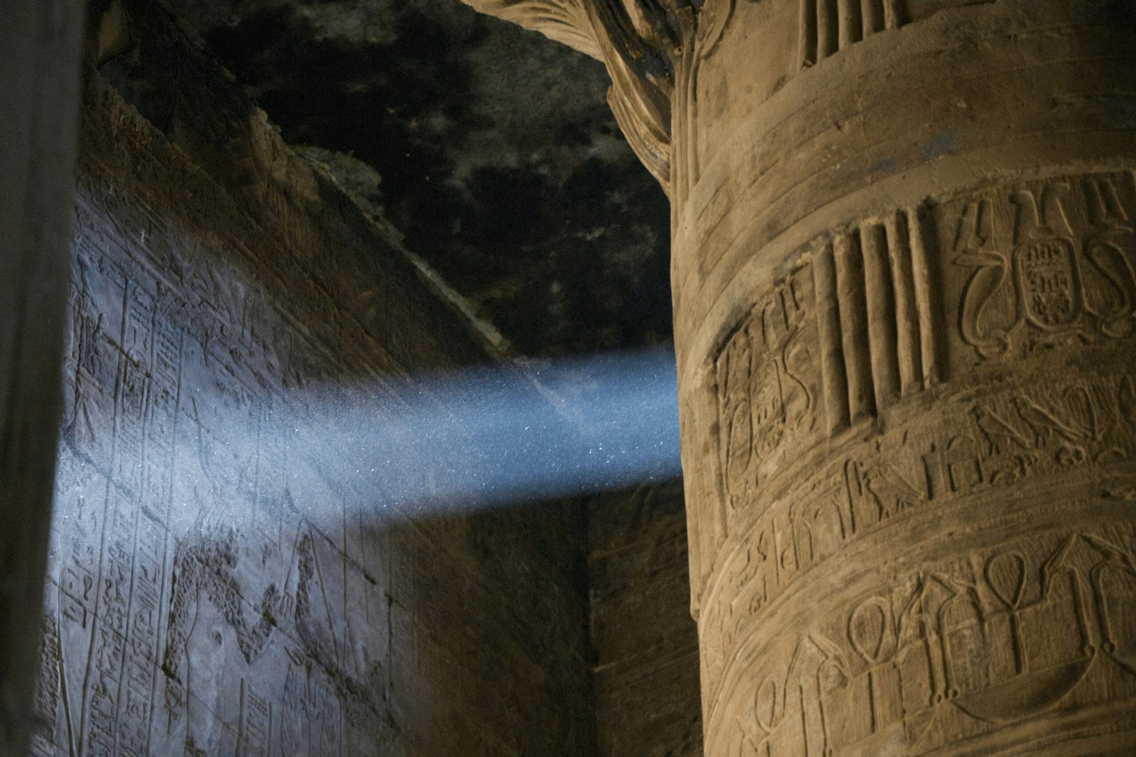 A photo of the interior of the Temple of Edfu, showcasing the towering columns, the hieroglyphics on the walls, and a beam of sunlight illuminating the space.