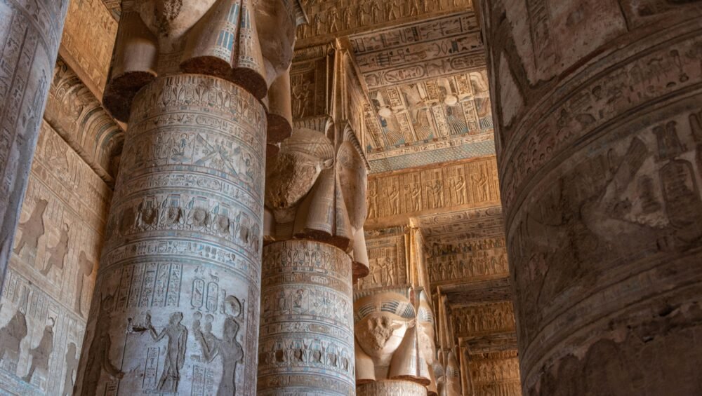 A photo of the interior of the Temple of Hathor in Dendera, showcasing the towering columns, the hieroglyphics on the walls, and the intricate ceiling paintings.