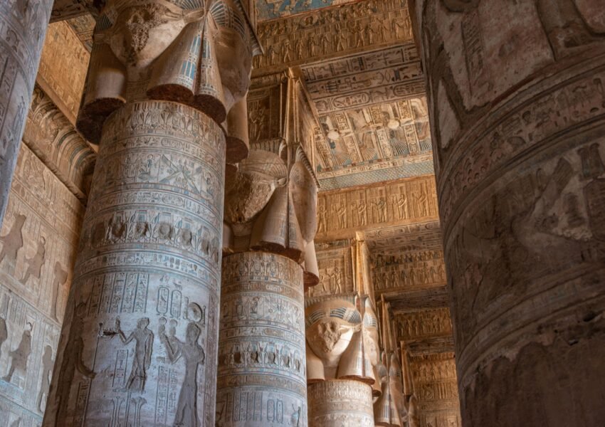 A photo of the interior of the Temple of Hathor in Dendera, showcasing the towering columns, the hieroglyphics on the walls, and the intricate ceiling paintings.