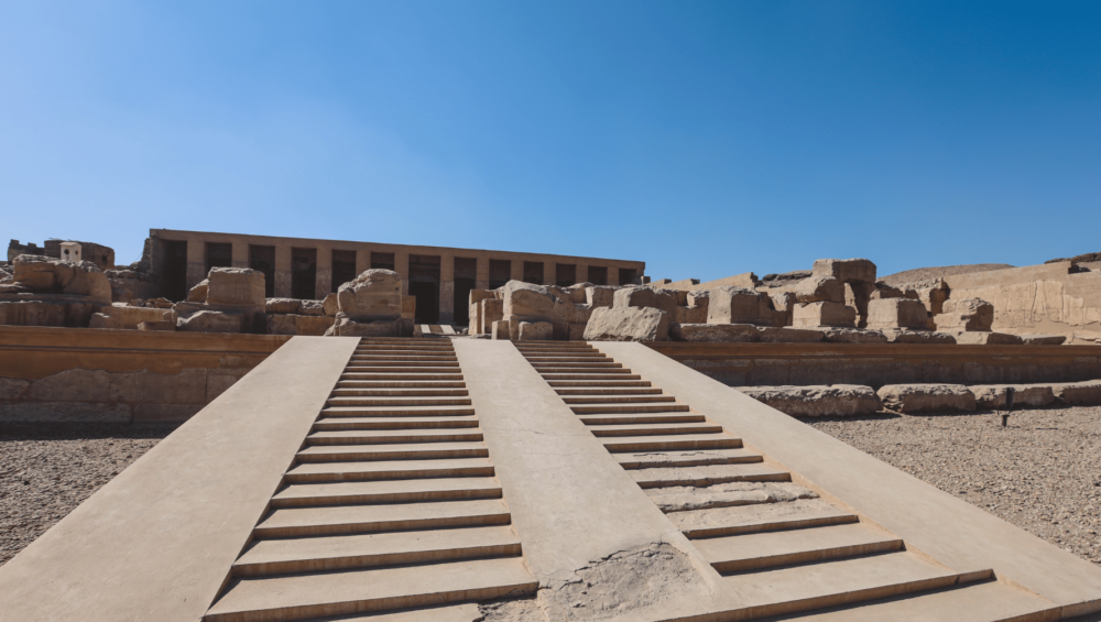 Front view of the Temple of Seti I in Abydos, Egypt, with stone steps leading to the entrance and ruins on both sides.