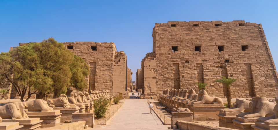 Entrance to Karnak Temple with the Avenue of Sphinxes under a blue sky.