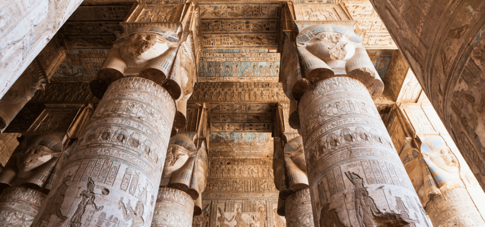 Intricately carved columns with Hathor capitals in the Temple of Hathor at Dendera, featuring detailed hieroglyphs and colorful depictions on the ceilings.