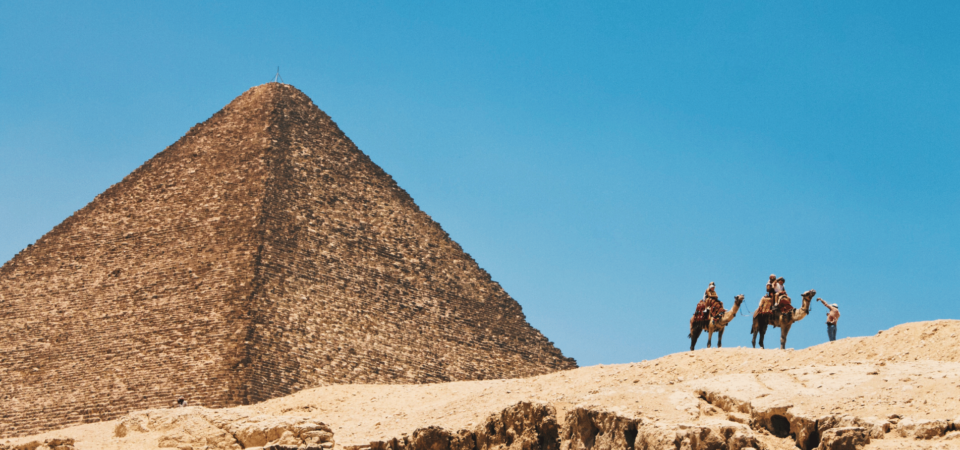 Camel riders near the Great Pyramid of Giza under a clear blue sky.