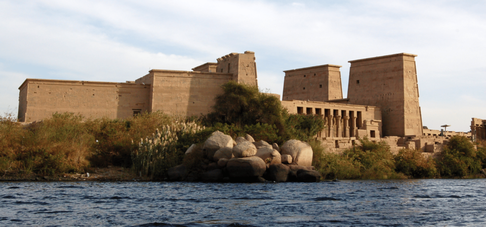 Temple of Isis at Philae surrounded by lush vegetation and the Nile River.