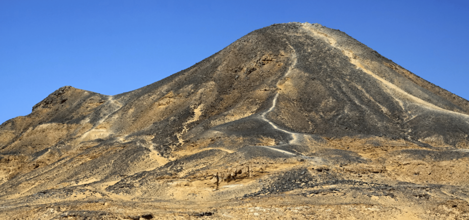 A striking view of the Black Mountain in Bahariya Oasis, with dark volcanic rock formations contrasting against the clear blue sky.