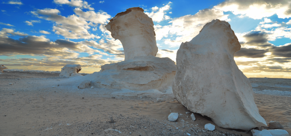 White rock formations shaped by wind erosion, resembling giant mushrooms, set against a vibrant sunset in Egypt’s White Desert.