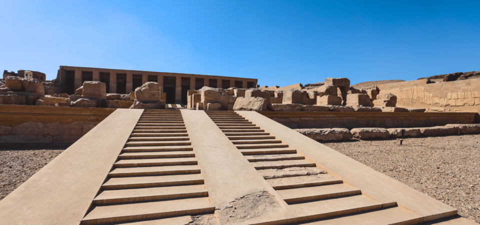 The front view of the Temple of Seti I in Abydos, featuring monumental steps leading to the ancient structure surrounded by ruins.