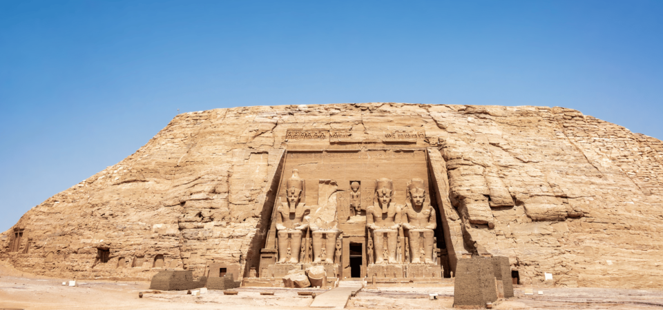 Abu Simbel Temple carved into a sandstone cliff under a bright blue sky.