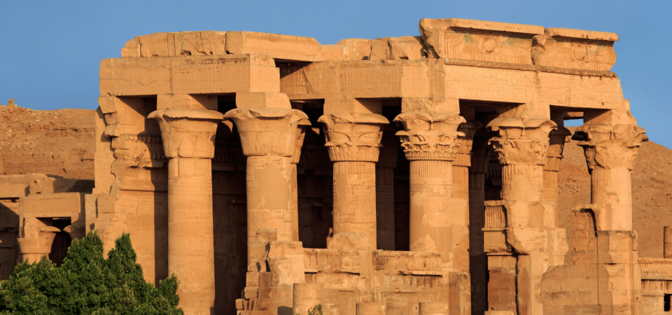 The Temple of Sobek (Kom Ombo Temple) stands gracefully in the soft light of the setting sun, surrounded by lush greenery.