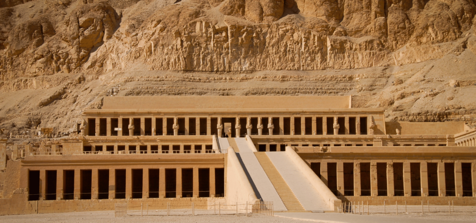 Mortuary Temple of Hatshepsut against desert cliffs in bright sunlight.