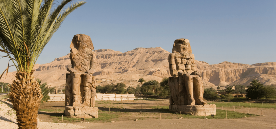 Two massive statues of Amenhotep III with desert mountains in the background.