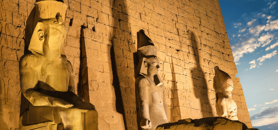 Statues at Luxor Temple illuminated under a starry night sky.