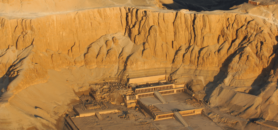 An aerial view of the Mortuary Temple of Hatshepsut nestled against dramatic cliffs in the desert.