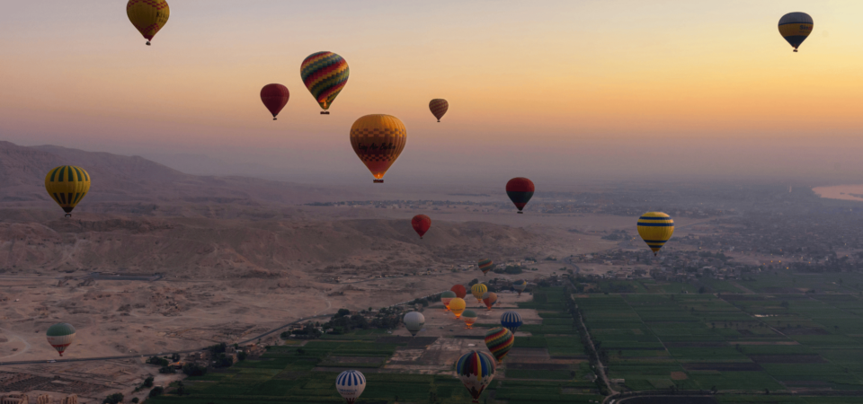 Colorful hot air balloons floating over Luxor at sunrise.