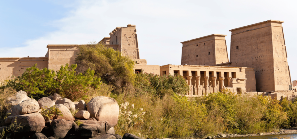 Philae Temple surrounded by lush greenery and reflected on the Nile River.