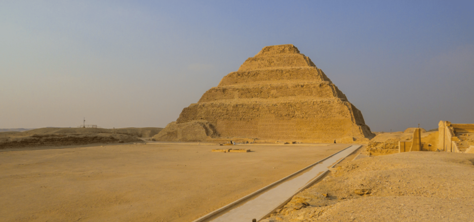 The Step Pyramid of Djoser in Saqqara surrounded by the expansive desert under a pale blue sky.