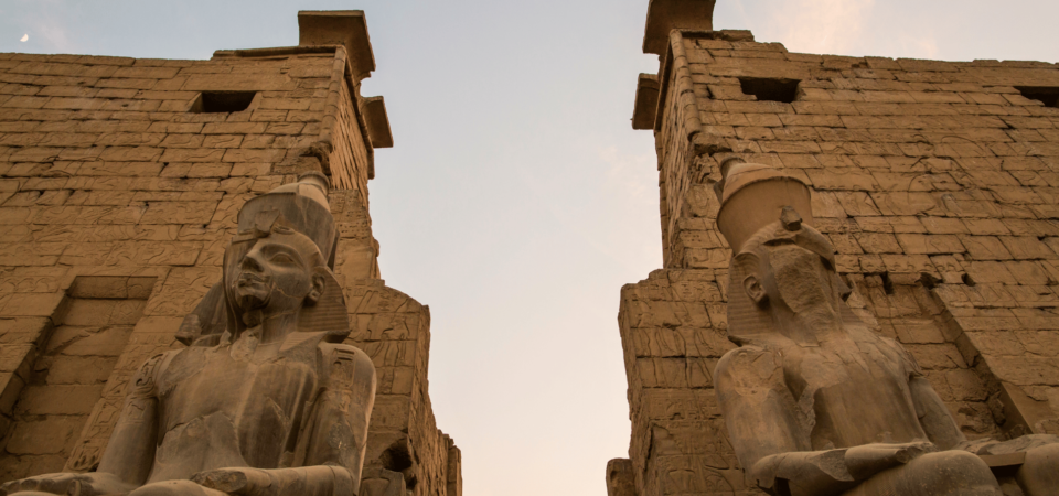 The colossal seated statues of Ramses II at Luxor Temple's entrance during sunset.