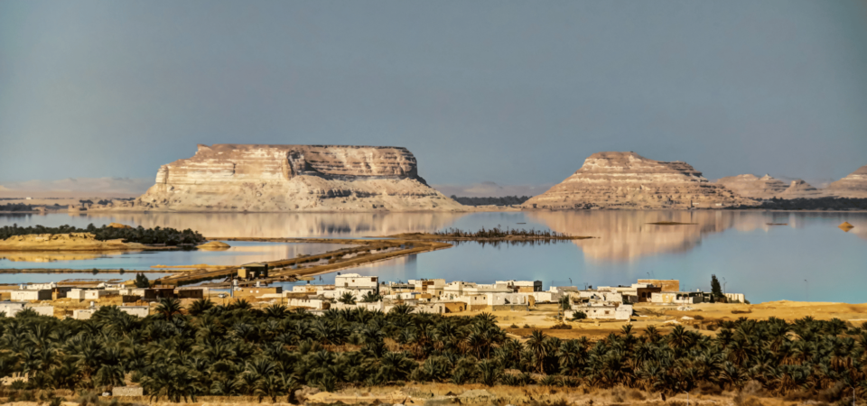 Crystal-clear waters reflecting serene mountains and desert landscapes at the Siwa Oasis.